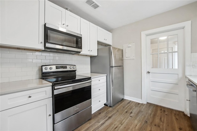 kitchen with white cabinets, hardwood / wood-style floors, backsplash, and stainless steel appliances