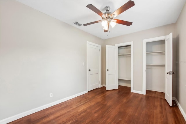 unfurnished bedroom with ceiling fan, dark wood-type flooring, and multiple closets