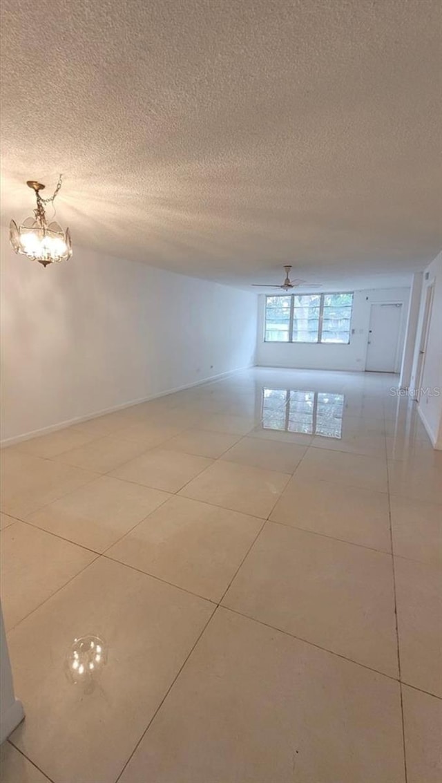 tiled empty room with a textured ceiling and ceiling fan with notable chandelier