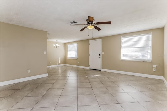 tiled empty room with ceiling fan with notable chandelier