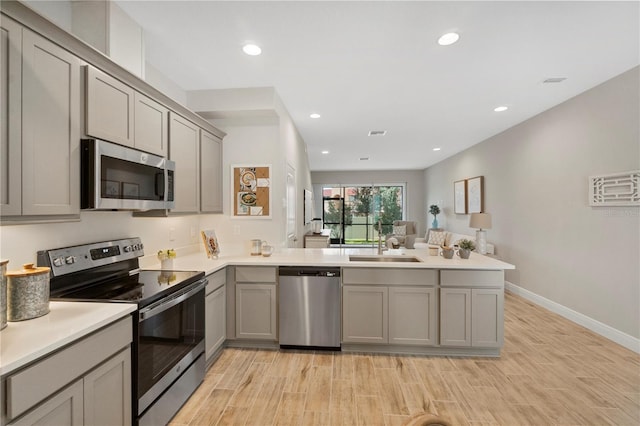 kitchen featuring sink, stainless steel appliances, light hardwood / wood-style flooring, kitchen peninsula, and gray cabinets