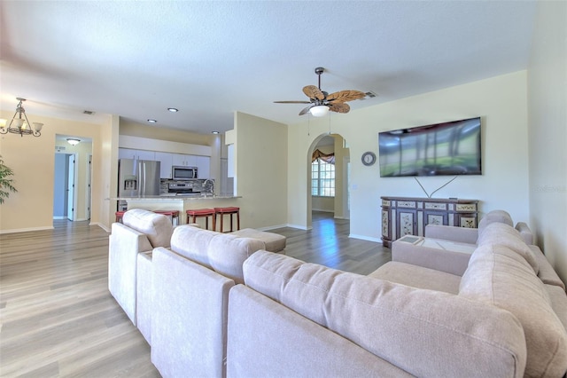 living room featuring ceiling fan with notable chandelier and light wood-type flooring