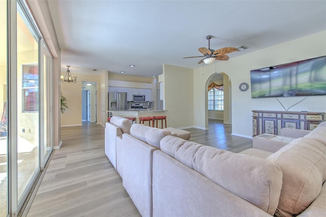 living room featuring ceiling fan with notable chandelier, light wood-type flooring, and sink