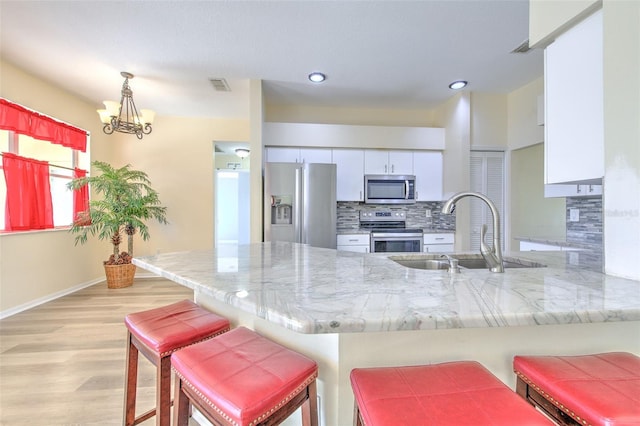 kitchen featuring kitchen peninsula, appliances with stainless steel finishes, sink, an inviting chandelier, and white cabinets