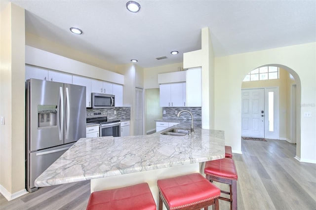 kitchen featuring backsplash, white cabinets, sink, appliances with stainless steel finishes, and a breakfast bar area