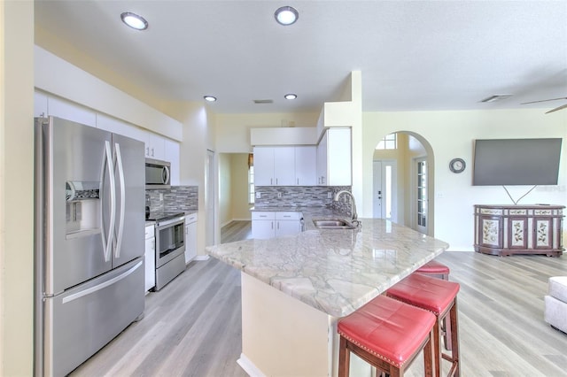 kitchen with sink, stainless steel appliances, a kitchen breakfast bar, decorative backsplash, and light wood-type flooring