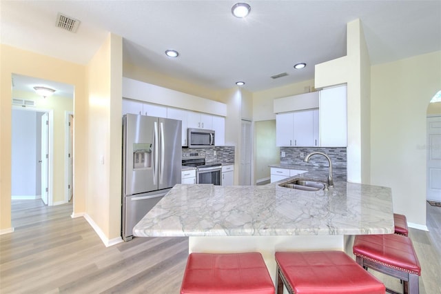 kitchen featuring white cabinetry, sink, kitchen peninsula, a breakfast bar area, and appliances with stainless steel finishes