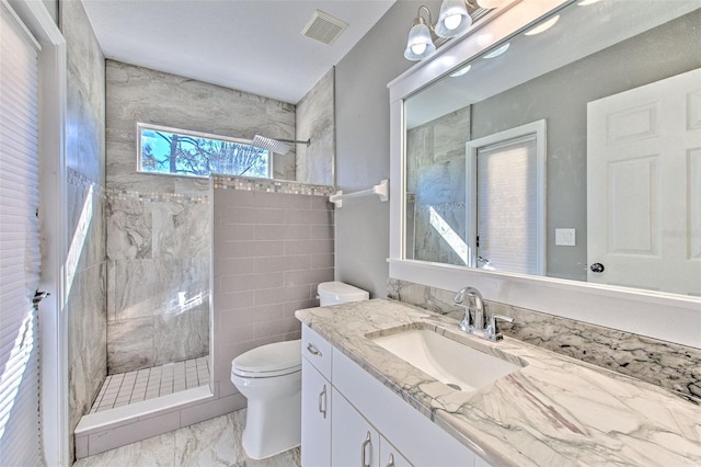 bathroom featuring a tile shower, vanity, tile walls, and toilet