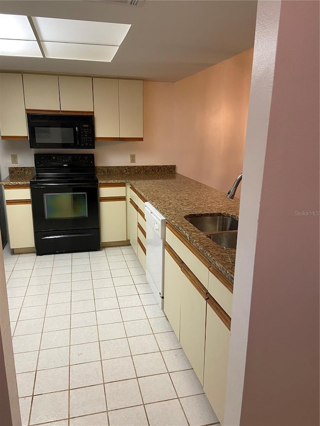 kitchen featuring dark stone counters, cream cabinets, black appliances, and sink