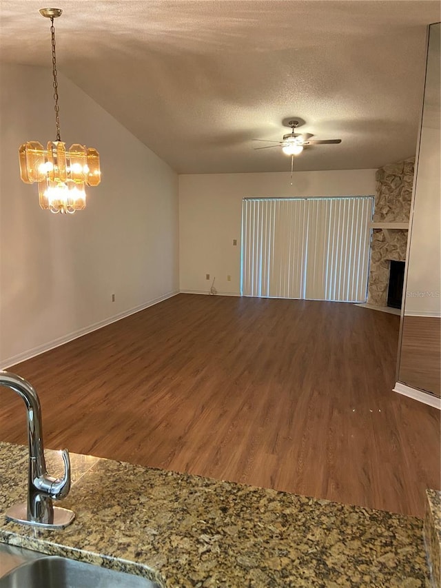 unfurnished living room featuring lofted ceiling, dark wood-type flooring, ceiling fan with notable chandelier, a textured ceiling, and a fireplace