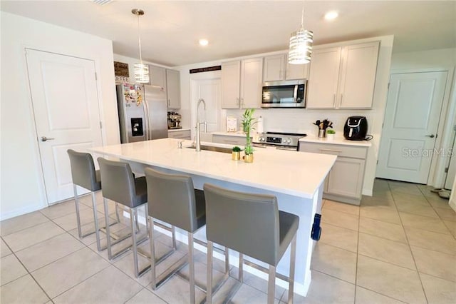 kitchen featuring gray cabinetry, a center island with sink, hanging light fixtures, light tile patterned floors, and appliances with stainless steel finishes