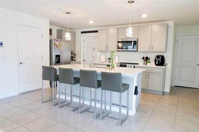 kitchen featuring appliances with stainless steel finishes, sink, a center island with sink, hanging light fixtures, and light tile patterned flooring