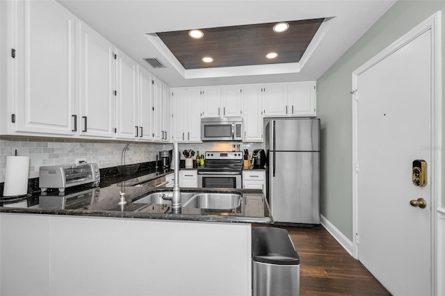 kitchen featuring stainless steel appliances, a raised ceiling, dark hardwood / wood-style floors, kitchen peninsula, and white cabinets