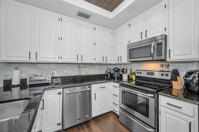 kitchen with appliances with stainless steel finishes, backsplash, white cabinetry, and dark stone counters