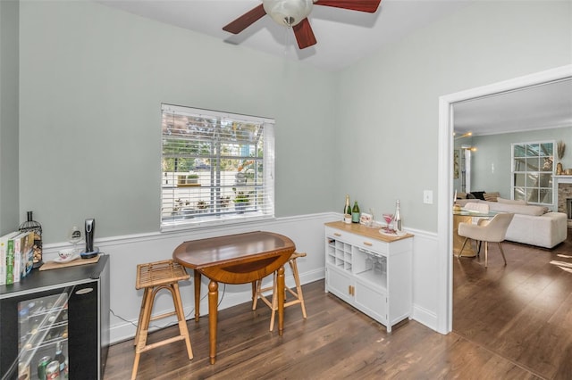 interior space featuring a stone fireplace, beverage cooler, dark wood-type flooring, and ceiling fan