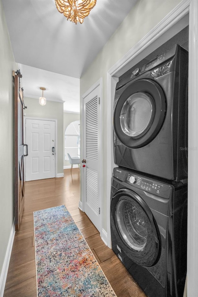 clothes washing area with stacked washer / dryer, a barn door, and hardwood / wood-style flooring