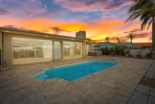 pool at dusk with a jacuzzi and a patio