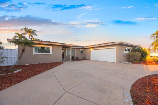 ranch-style home featuring stucco siding, a garage, driveway, and fence