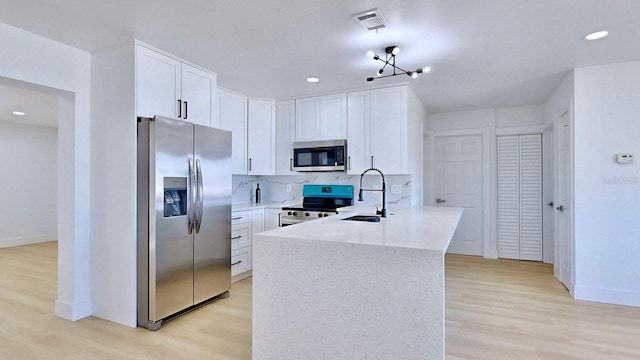 kitchen with appliances with stainless steel finishes, light hardwood / wood-style floors, white cabinetry, and a notable chandelier