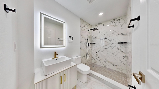 bathroom with a tile shower, vanity, and toilet