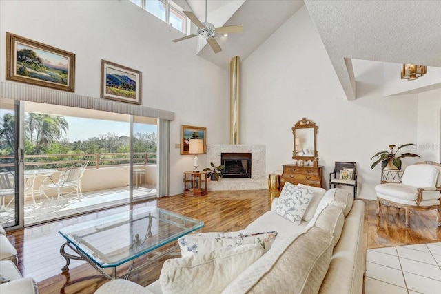 living room with ceiling fan, a high end fireplace, high vaulted ceiling, a textured ceiling, and light wood-type flooring