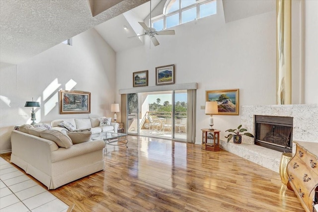 living room with ceiling fan, a premium fireplace, high vaulted ceiling, light hardwood / wood-style floors, and a textured ceiling