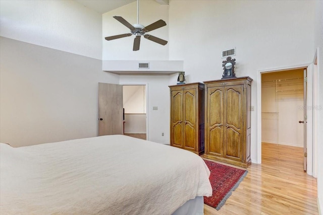 bedroom with a walk in closet, ceiling fan, light hardwood / wood-style flooring, high vaulted ceiling, and a closet