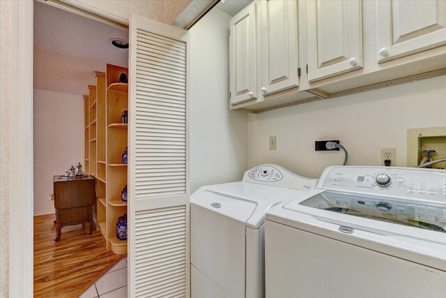 laundry area featuring washing machine and clothes dryer, light tile patterned floors, cabinets, and a textured ceiling