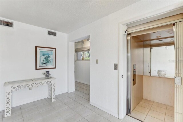 hall featuring light tile patterned floors, a textured ceiling, and elevator