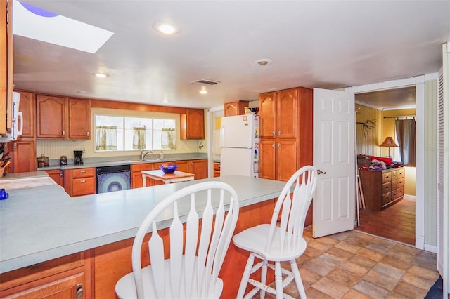 kitchen with a skylight, sink, kitchen peninsula, white appliances, and a breakfast bar area