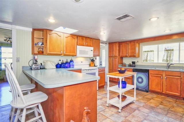 kitchen with sink, kitchen peninsula, white appliances, washer / dryer, and a kitchen bar