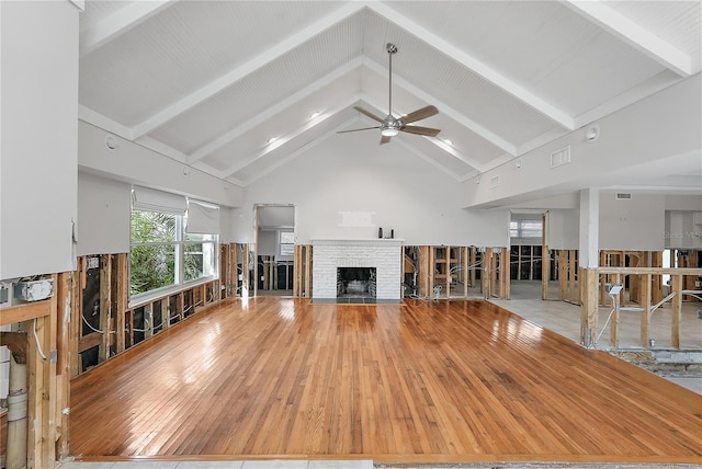 unfurnished living room with ceiling fan, a brick fireplace, beam ceiling, light hardwood / wood-style flooring, and high vaulted ceiling