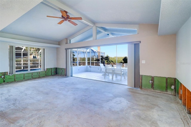 unfurnished living room with ceiling fan, a wealth of natural light, a textured ceiling, and vaulted ceiling with beams