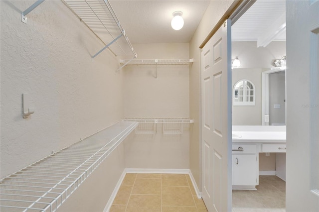 walk in closet with beamed ceiling and light tile patterned floors