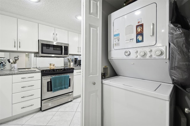 kitchen with light tile patterned floors, stacked washing maching and dryer, a textured ceiling, appliances with stainless steel finishes, and white cabinetry