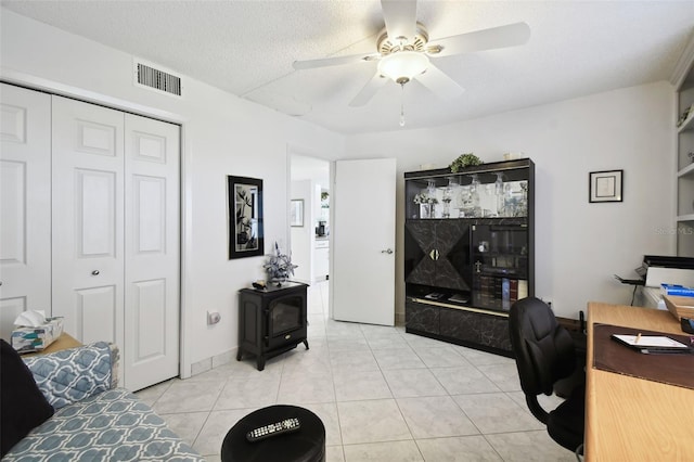 tiled office space featuring ceiling fan, a wood stove, and a textured ceiling