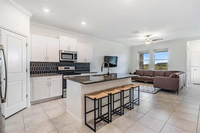 kitchen featuring white cabinets, an island with sink, appliances with stainless steel finishes, and dark stone counters