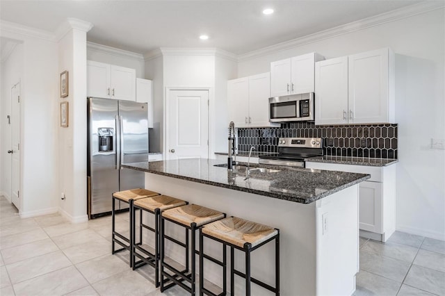 kitchen featuring appliances with stainless steel finishes, tasteful backsplash, sink, white cabinetry, and an island with sink