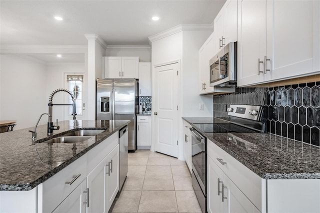 kitchen featuring dark stone counters, stainless steel appliances, a kitchen island with sink, sink, and white cabinets