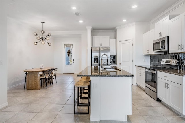 kitchen featuring sink, dark stone countertops, an island with sink, appliances with stainless steel finishes, and white cabinetry