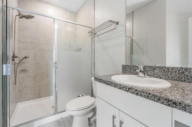 bathroom featuring tile patterned flooring, vanity, a shower with shower door, and toilet