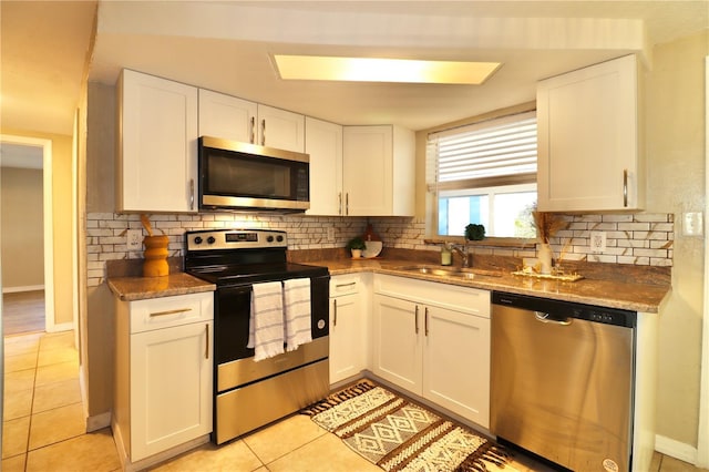 kitchen featuring appliances with stainless steel finishes, tasteful backsplash, sink, light tile patterned floors, and white cabinetry