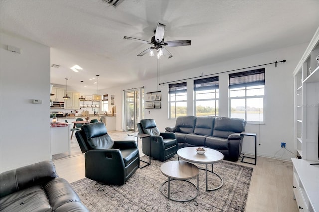 living room with ceiling fan, a textured ceiling, and light wood-type flooring