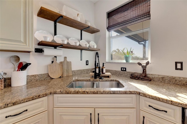 kitchen featuring light stone counters, sink, and white cabinetry