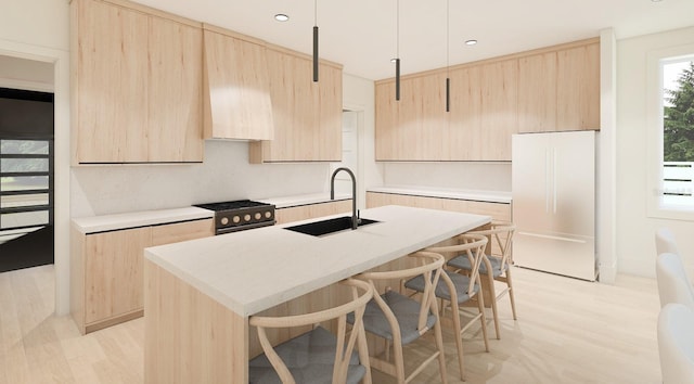 kitchen with light brown cabinets, a kitchen island with sink, white refrigerator, sink, and stainless steel stove