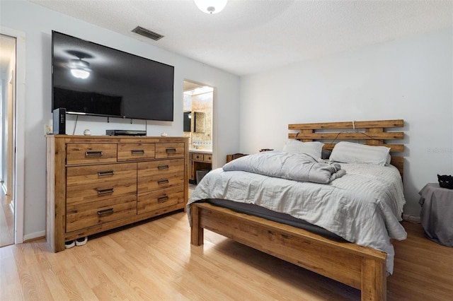 bedroom with a textured ceiling, connected bathroom, and light hardwood / wood-style floors