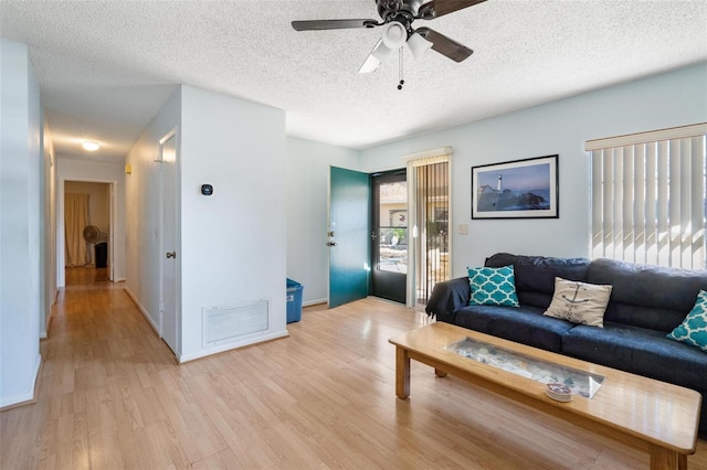 living room featuring ceiling fan, light hardwood / wood-style flooring, and a textured ceiling