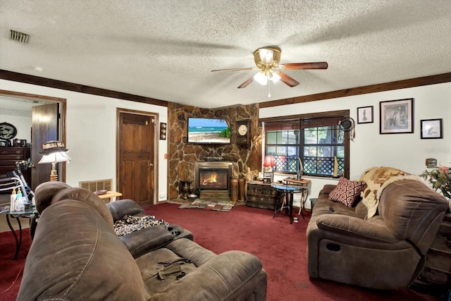 living room featuring carpet, a stone fireplace, crown molding, ceiling fan, and a textured ceiling