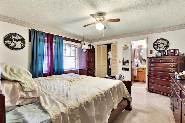 bedroom with a textured ceiling, light colored carpet, ensuite bath, and ceiling fan