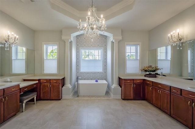 bathroom featuring a tub to relax in, a raised ceiling, ornate columns, and a healthy amount of sunlight